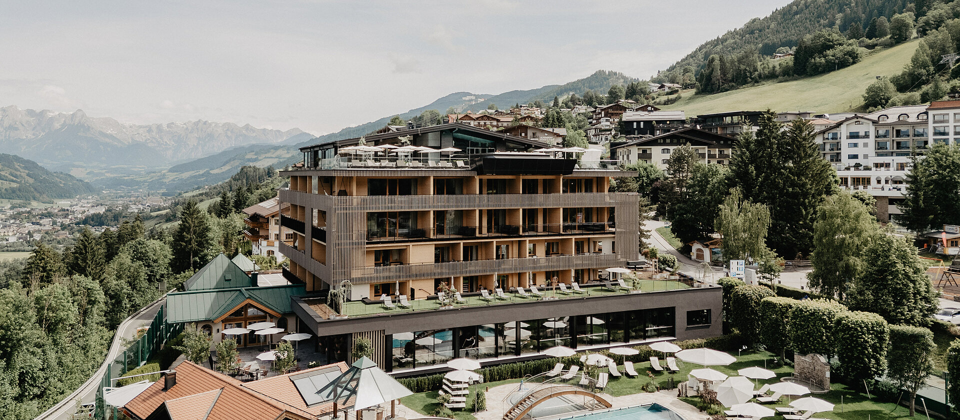 Außenaufnahme des Hotel Berghof in Salzburg mit Pool, Liegewiese, Sonnenschirmen und Bergpanorama im Sommer.