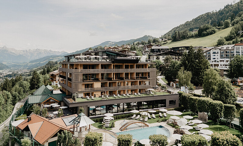 Außenaufnahme des Hotel Berghof in Salzburg mit Pool, Liegewiese, Sonnenschirmen und Bergpanorama im Sommer.