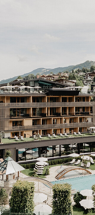 Außenaufnahme des Hotel Berghof in Salzburg mit Pool, Liegewiese, Sonnenschirmen und Bergpanorama im Sommer.