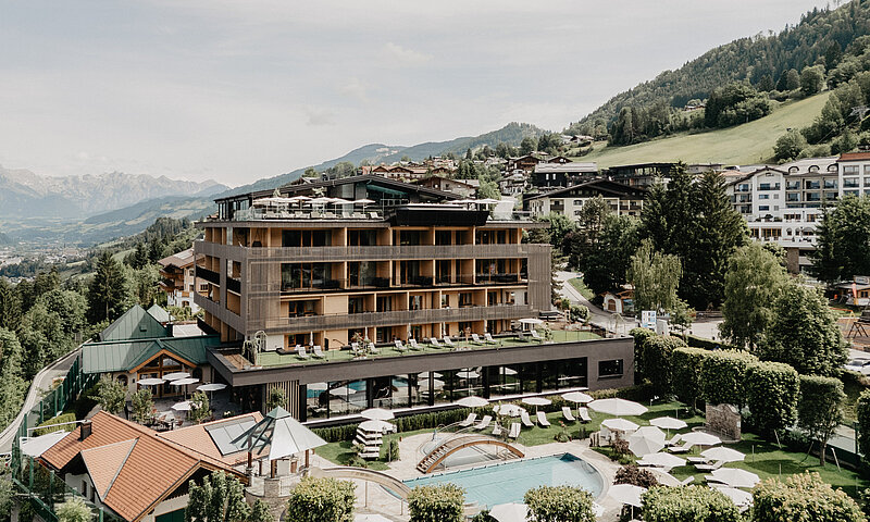 Außenaufnahme des Hotel Berghof in Salzburg mit Pool, Liegewiese, Sonnenschirmen und Bergpanorama im Sommer.