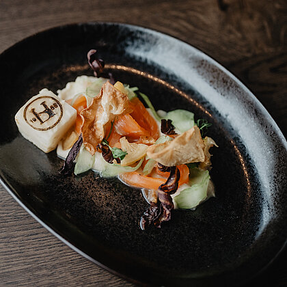 Eine leichte Vorspeise mit Gurke und frischem Lachs auf einem schwarzen Teller angerichtet.