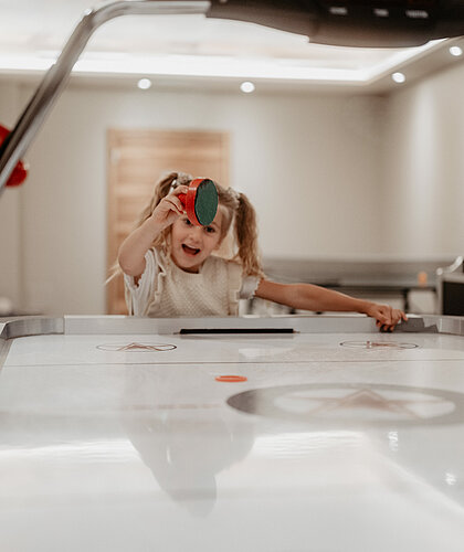 Ein Kind lacht beim Air Hockey spielen im Gaming Room des Hotel Berghof.