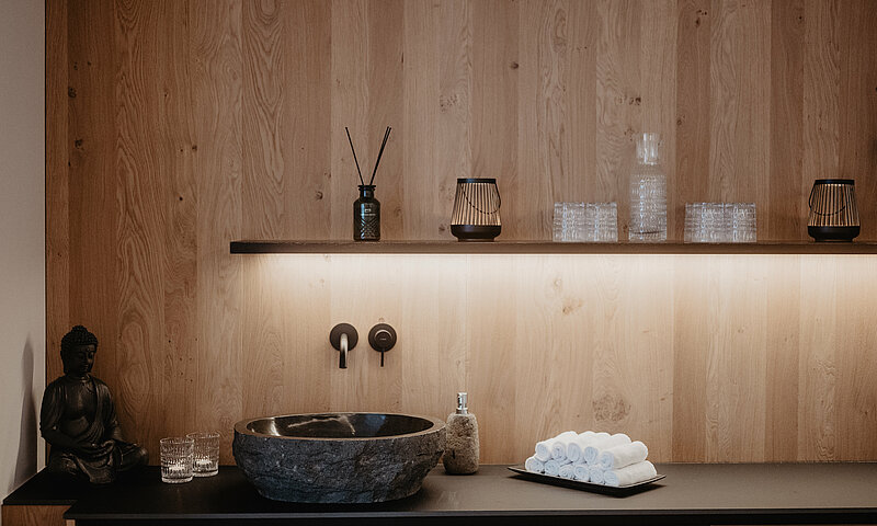 Stilvoll gestalteter Waschbereich im Wellnessbereich des Hotel Berghof mit Natursteinbecken, Handtüchern und Holzverkleidung.