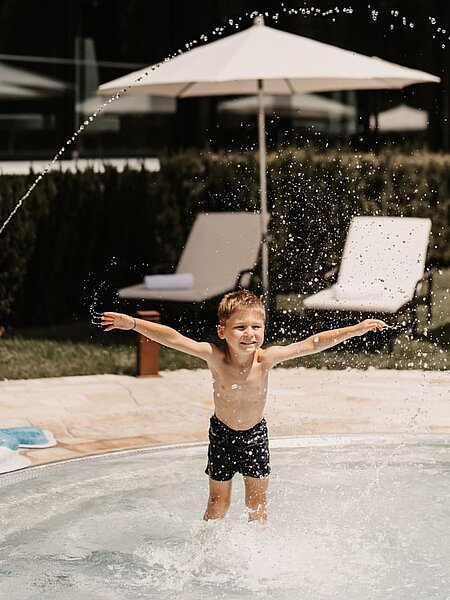 Kleiner Junge spritzt mit Wasser um sich und amüsiert sich dabei