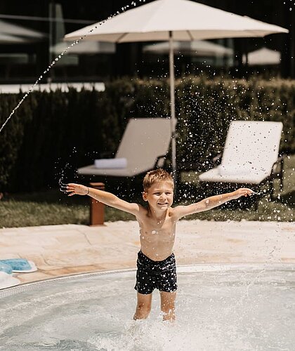 Kleiner Junge spritzt mit Wasser um sich und amüsiert sich dabei