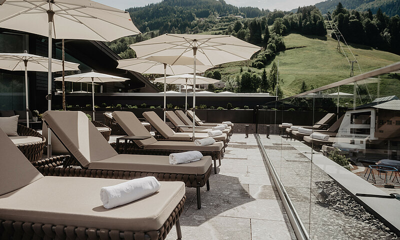 Sonnenliegen mit Handtüchern und Sonnenschirmen auf der Rooftop-Terrasse des Wellnesshotels Berghof in Salzburg.