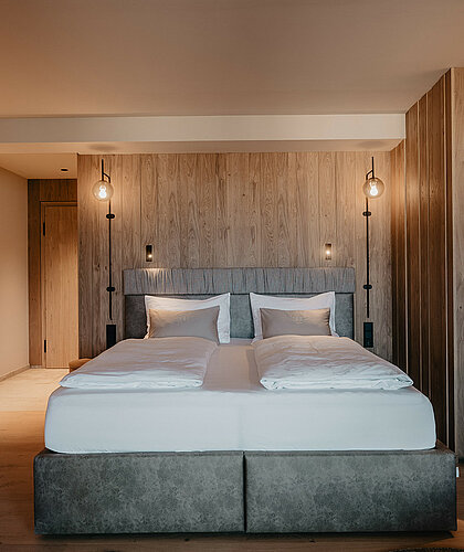 Schlafbereich der Berghof Suite Premium mit großem Doppelbett, Holzverkleidung und stilvollem Ambiente im Hotel Berghof Salzburg.