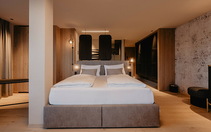 Gemütlicher Schlafbereich einer Suite mit hochwertigem Doppelbett, eleganter Holzverkleidung und modernem Design im Hotel Berghof Salzburg.