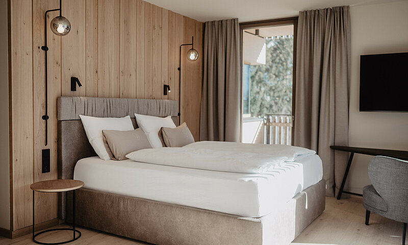 Boxspringbett in hellem Zimmer vor Holzwand.