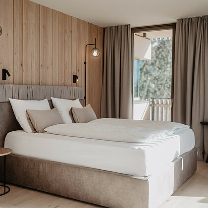 Boxspringbett in hellem Zimmer vor Holzwand.