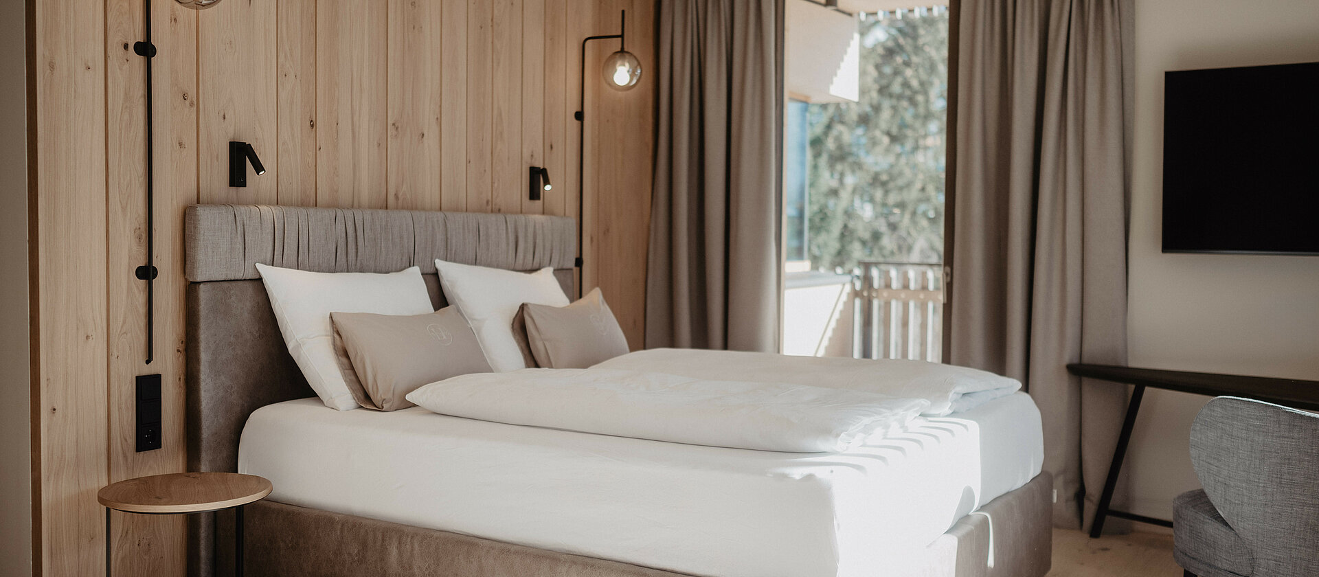 Boxspringbett in hellem Zimmer vor Holzwand.