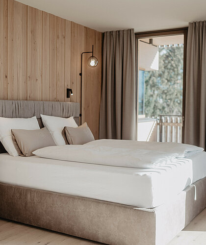 Boxspringbett in hellem Zimmer vor Holzwand.