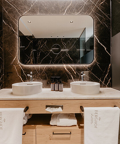 Elegantes Badezimmer der Premium Familiensuite mit Doppelwaschbecken, beleuchtetem Spiegel und edler Marmorgestaltung.