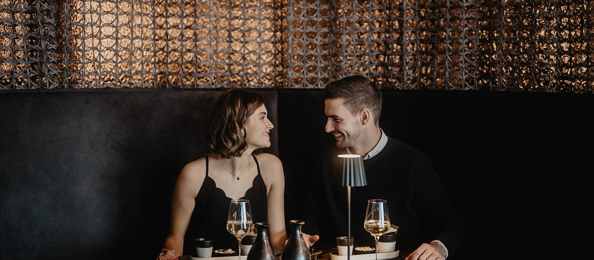 Zwei Personen schauen sich verliebt an vor dunkler Kulisse im Restaurant Medusa im Hotel Berghof.