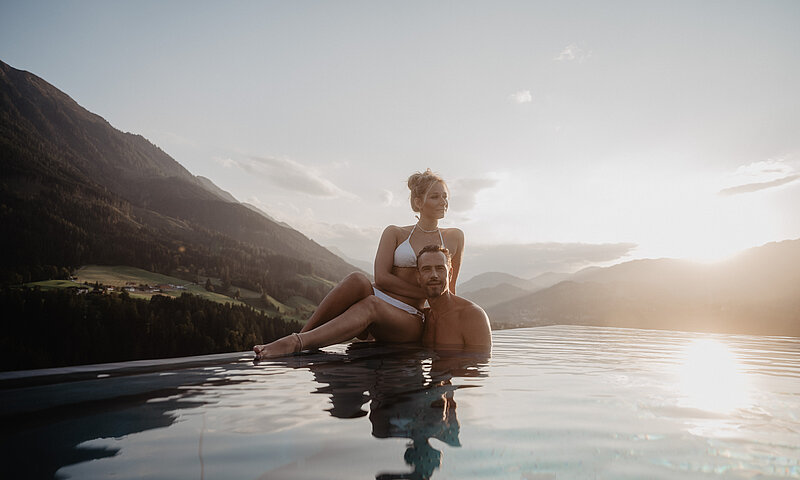 Paar entspannt im Infinitypool und genießt den Sonnenuntergang mit Bergpanorama im Hotel Berghof Salzburg