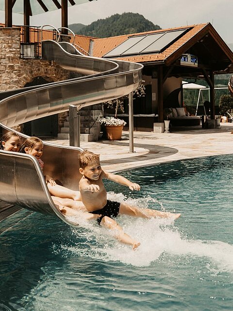 Kinder rutschen bei der Wasserrutsche am Outdoor Pool und haben Spaß