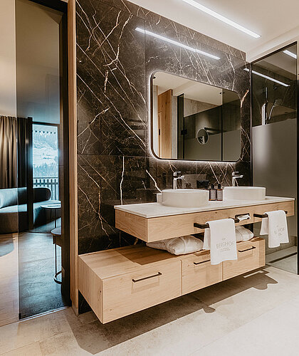 Modernes Badezimmer der Junior Suite Premium mit Doppelwaschbecken, edlem Marmor-Design und beleuchtetem Spiegel.