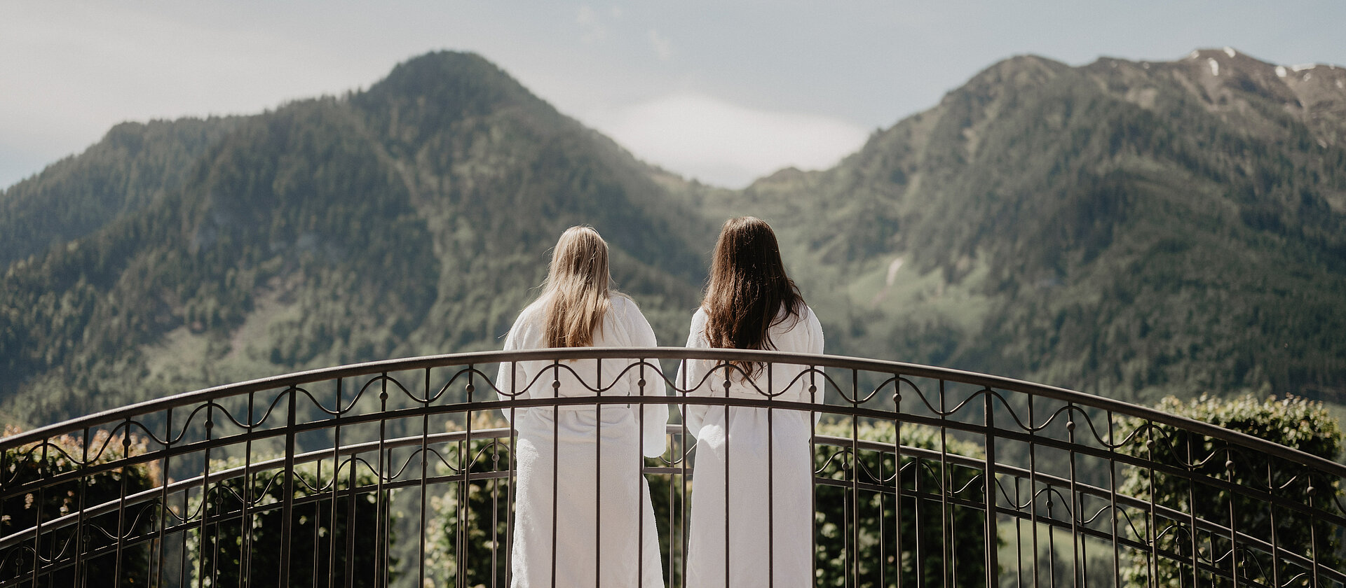 Zwei Frauen im Bademantel auf der Brücke mit Blick auf die Berge am Hotel Berghof Salzburg.