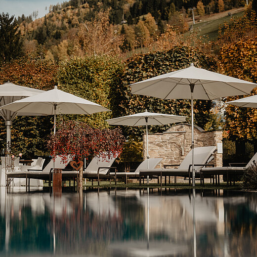 Ein Pool mit Sonnenschirmen am Rand und herbstlicher Kulisse im Hintergrund.