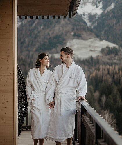 Paar im Bademantel spaziert am Balkon und unterhält sich.