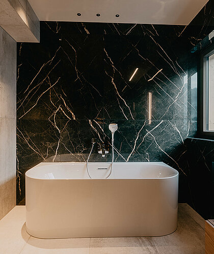 Badewanne im Badezimmer der Top Familiensuite mit schwarzer Marmorwand und Fenster im Hotel Berghof Salzburg.