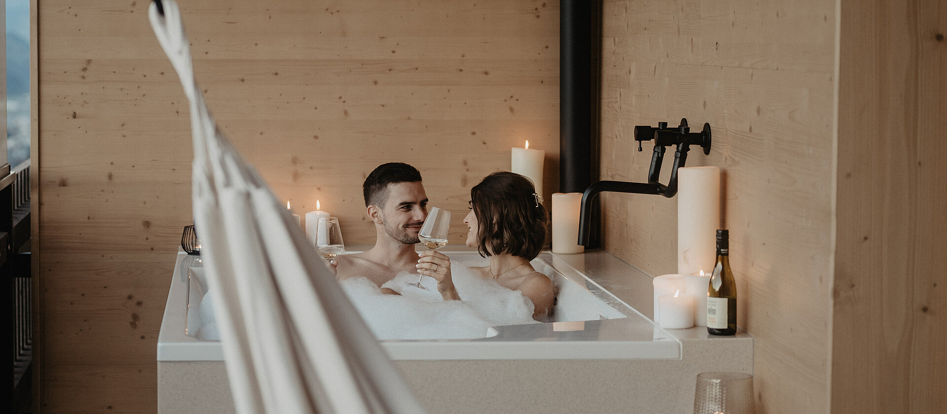 Ein Paar im Schaumbad auf freistehender Badewanne am Balkon.