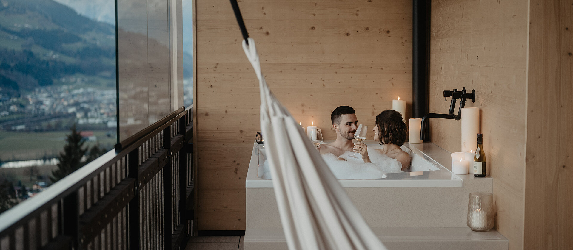 Ein Paar im Schaumbad auf freistehender Badewanne am Balkon.