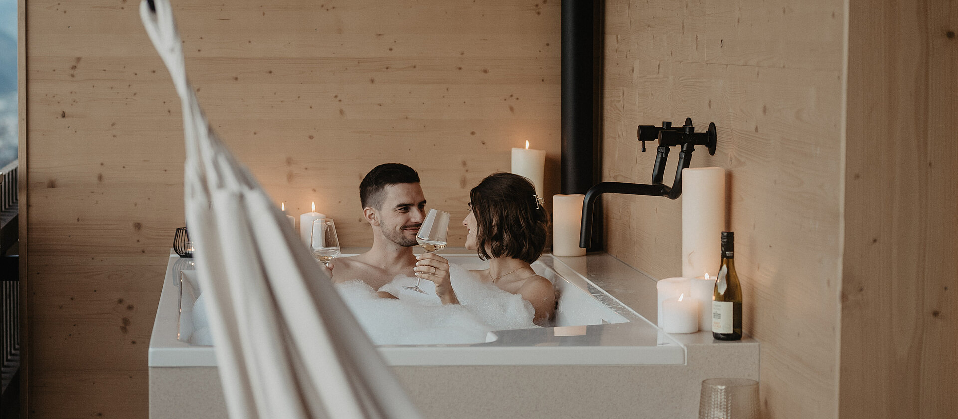 Ein Paar im Schaumbad auf freistehender Badewanne am Balkon.