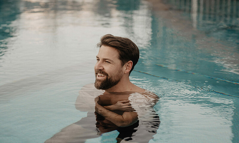 Ein Mann ist im Wasser im Outdoor Pool, das Wasser ist türkisblau.