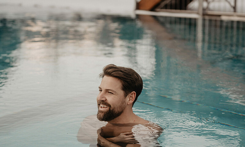 Ein Mann ist im Wasser im Outdoor Pool, das Wasser ist türkisblau.