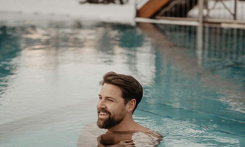 Ein Mann ist im Wasser im Outdoor Pool, das Wasser ist türkisblau.