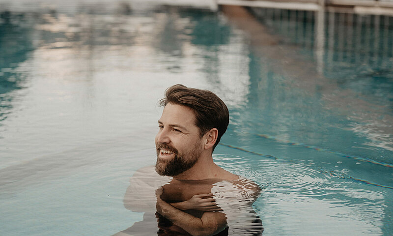 Ein Mann ist im Wasser im Outdoor Pool, das Wasser ist türkisblau.
