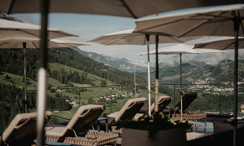 Sonnenliegen und Sonnenschirme auf der Rooftop-Terrasse des Wellnesshotels Berghof in Salzburg mit traumhaftem Blick auf die Berge.