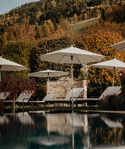 Ein Pool mit Sonnenschirmen am Rand und herbstlicher Kulisse im Hintergrund.