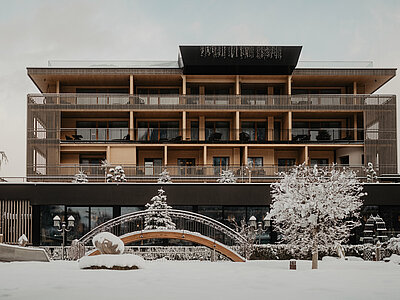 Frontansicht des Hotel Berghof in St. Johann im Winter, mit verschneitem Garten und moderner Architektur vor den Alpen in Österreich.