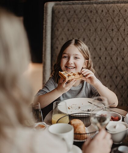 Ein fröhliches Kind isst eine Waffel beim Frühstück im Hotel Berghof.