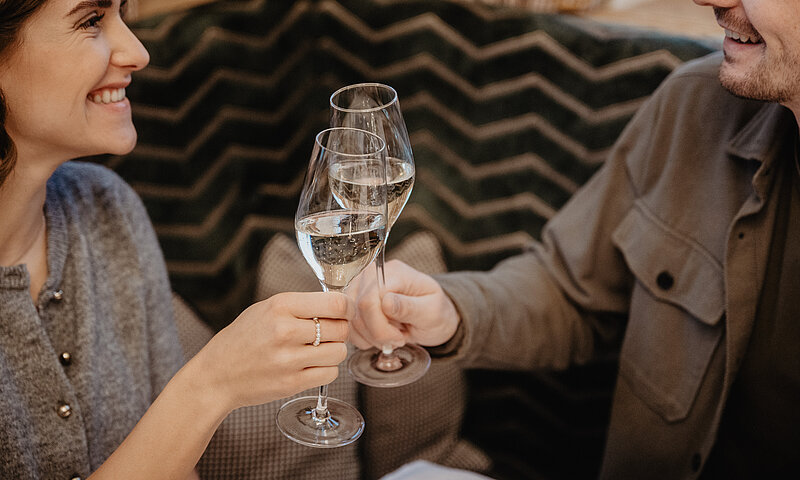 Paar stößt beim Frühstück mit Prosecco an, umgeben von gemütlichem Ambiente im Hotel Berghof in St. Johann, Salzburg