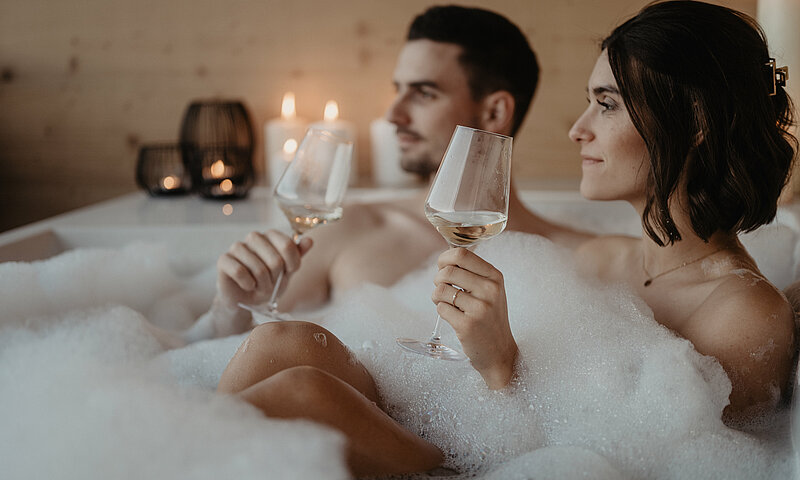 Entspannung im Schaumbad mit Weingläsern und Kerzenlicht.