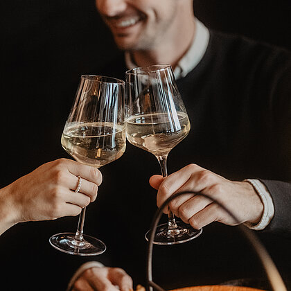 Zwei Personen die miteinander anstoßen mit einem Glas Wein und sich verliebt in die Augen schauen.