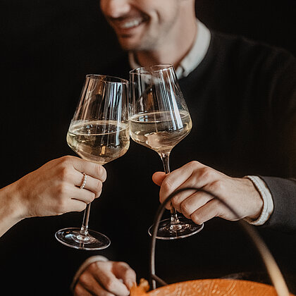 Zwei Personen die miteinander anstoßen mit einem Glas Wein und sich verliebt in die Augen schauen.