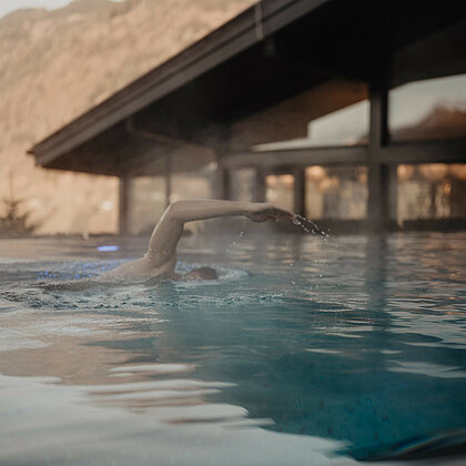 Mann krault entspannt im Infinity-Pool mit Blick auf die Salzburger Berge.