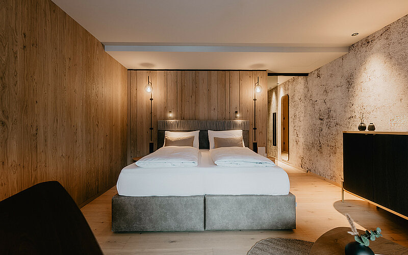 Hochwertiges Doppelbett mit Boxspringmatratzen in der Junior Suite Premium, umgeben von stilvoller Holzverkleidung und sanfter Beleuchtung.