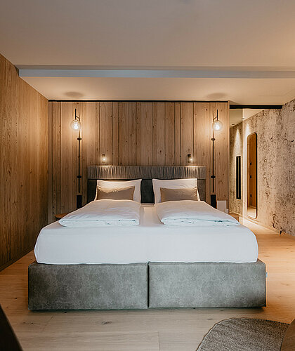 Hochwertiges Doppelbett mit Boxspringmatratzen in der Junior Suite Premium, umgeben von stilvoller Holzverkleidung und sanfter Beleuchtung.