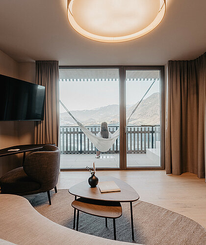 Gemütlicher Wohnbereich der Panorama Suite Premium mit moderner Einrichtung, großer Couch, Schreibtisch und Panoramafenstern im Hotel Berghof in Salzburg.