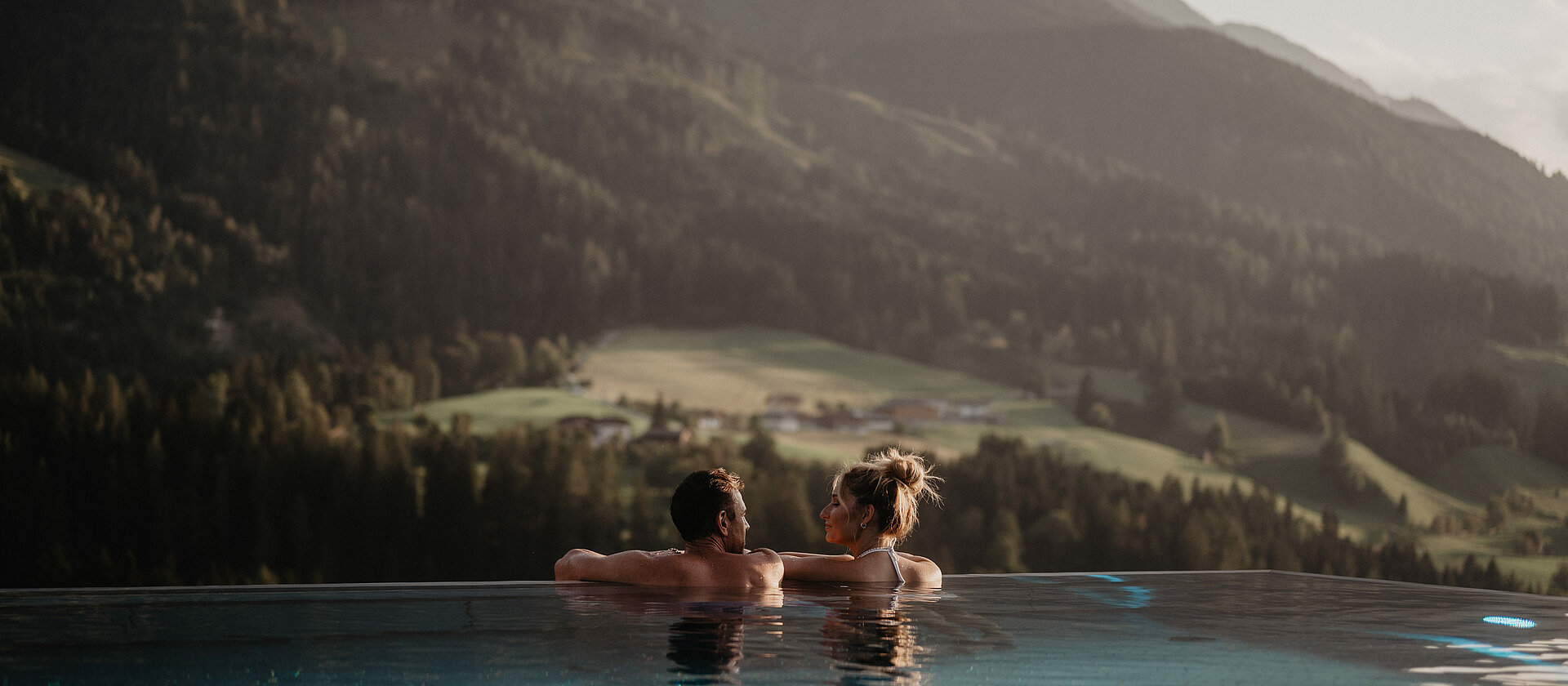 Paar entspannt im Infinitypool und blickt auf das Bergpanorama bei St. Johann im Hotel Berghof Salzburg