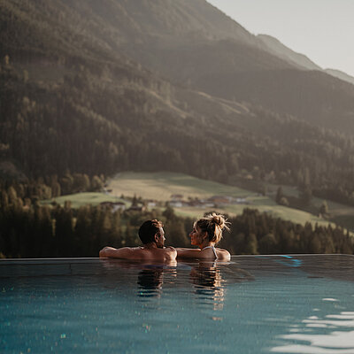 Paar entspannt im Infinitypool und blickt auf das Bergpanorama bei St. Johann im Hotel Berghof Salzburg