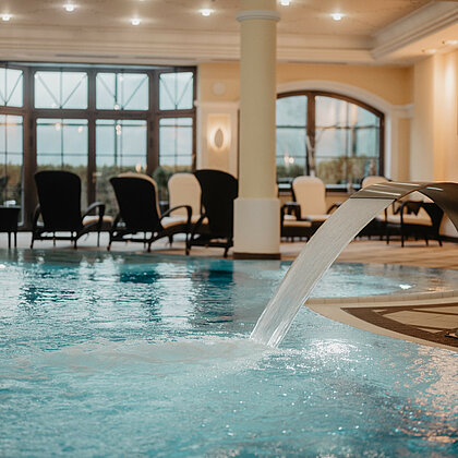 Blick auf den eleganten Pool mit Wasserfall und gemütlichen Liegestühlen im Hintergrund.