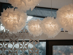 Moderne, wolkenartige Lampen im Ruheraum „Wolkennest“ vor einer dekorativen Wand und Fenstern.