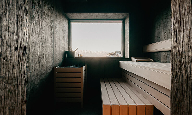Moderne Sauna mit Holzdesign und Panoramafenster mit freiem Blick auf die Alpenlandschaft im Hotel Berghof in Salzburg.