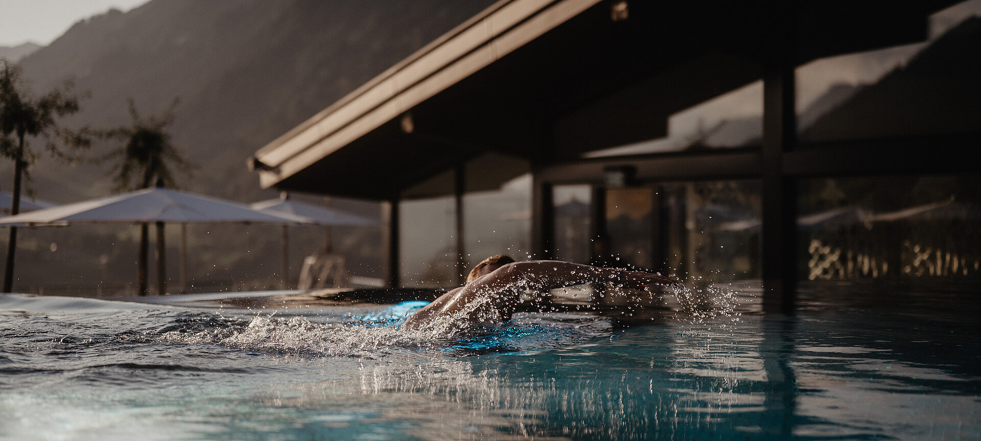 Jemand krault im Infinity Pool bei Sonnenuntergang im Hotel Berghof